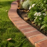 A brick garden edging outlining a garden bed with lush greenery.